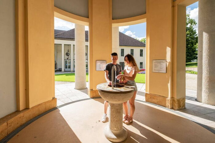 Heilwasserbrunnen im Brunnentempel mit Menschen und Blick auf das Comödienhaus