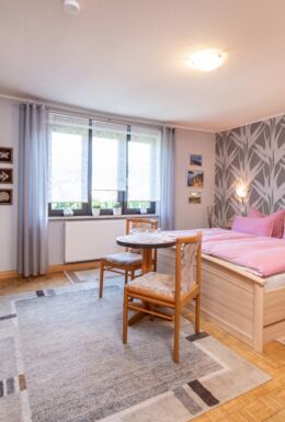 Innenaufnahme Zimmer mit Doppelbett, Kleiderschrank, TV, Tisch, Stühlen