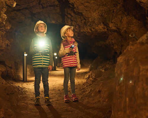 zwei Kinder mit Taschenlampe und Helm stehen in einer Höhle