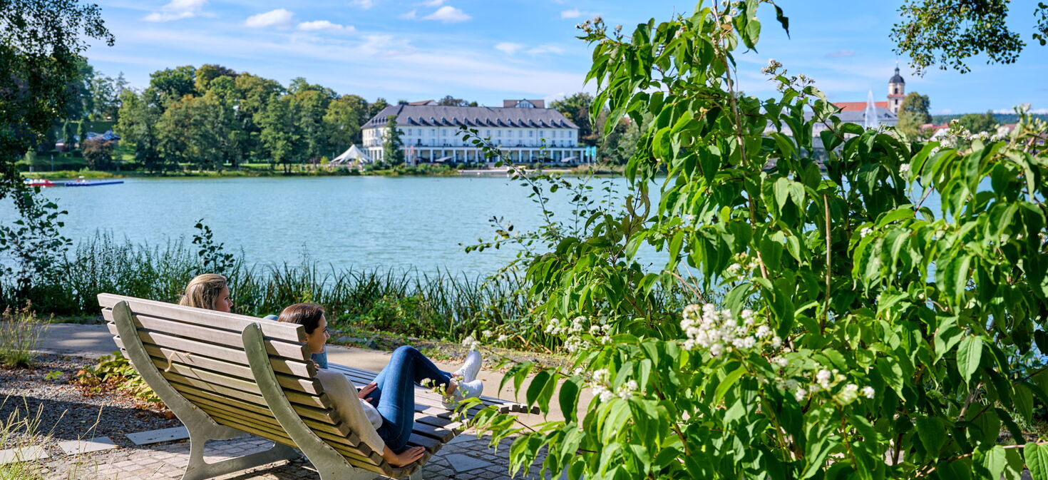 Zwei Frauen entspannen auf einer Bank mit Blick über den Burgsee Bad Salzungen zur Kurklinik