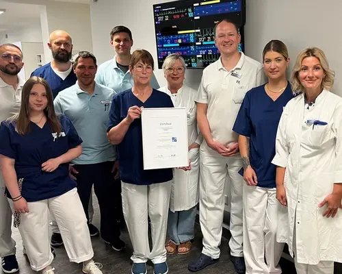 Gruppenbild: 10 Personen, in der Mitte hält eine Frau das Zertifikat in die Kamera